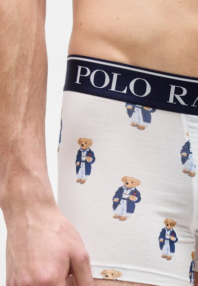 Λευκά μποξεράκια με μπλε σκούρο ελαστικό στη μέση που γράφει "POLO RALPH LAUREN" και μικρές στάμπες από αρκουδάκια που φορούν μπλε μπουφάν.