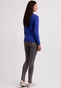 Modrý dlouhý rukáv top spárovaný se šedými slim jeans a bílými teniskami. Top má jednoduchý design a měkkou texturu.