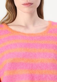 Strickpullover mit lockerer Passform, der horizontale Streifen in leuchtendem Pink und Orange aufweist, einen weiten Halsausschnitt hat und eine weiche, flauschige Textur besitzt.