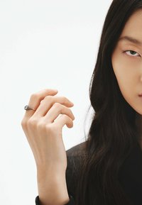 Anillo de plata con una piedra redonda, diseñado en una elegante espiral. La mano tiene una textura natural, mostrando dedos delicados contra un fondo neutro.