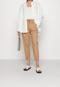 White oversized button-up shirt, beige drawstring pants with elastic cuffs, and white strappy sandals. Holding a gray clutch.