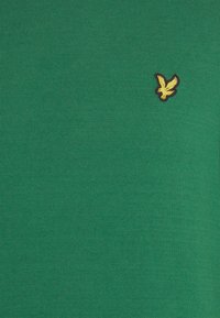 Zielony bawełniany t-shirt z krótkim rękawem, z małym złotym logo ptaka na lewej piersi, o gładkiej, prążkowanej fakturze.