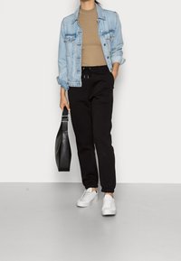Chaqueta de mezclilla azul claro, suéter de cuello alto beige, pantalones de chándal negros con cordón, zapatillas blancas y un bolso negro de hombro. Estilo minimalista.