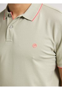 Lichtgroen polo shirt met een gestructureerde stof, twee knoopsluitingen en roze kraagaccenten. Heeft een klein logo op de borst.