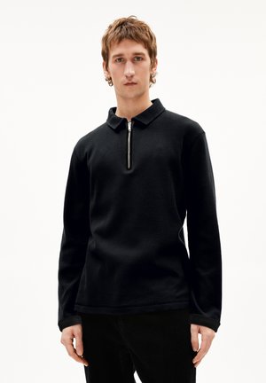 Black long-sleeve polo shirt with a textured fabric and a zippered collar. The design features a relaxed fit and contrasting cuff accents.