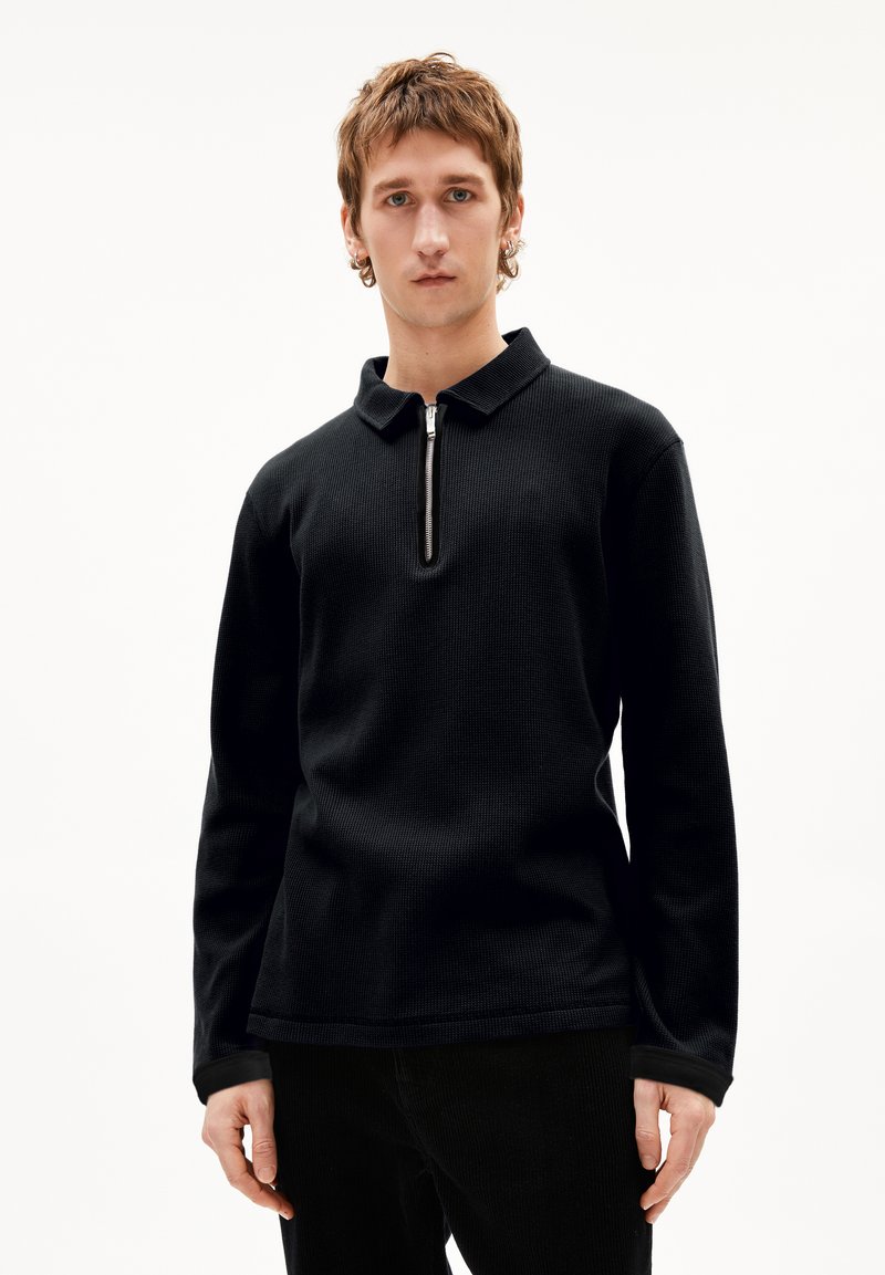 Schwarzes langärmliges Polohemd aus strukturiertem Stoff mit einem Reißverschlusskragen. Das Design zeichnet sich durch eine lockere Passform und kontrastierende Akzente an den Bündchen aus.