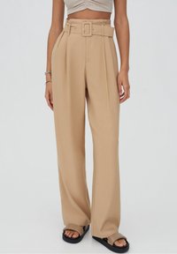 Pantalons beiges taille haute avec jambes larges, dotés d'une ceinture à l'avant et de plis. Fabriqués dans un tissu lisse avec un design épuré et taillé.