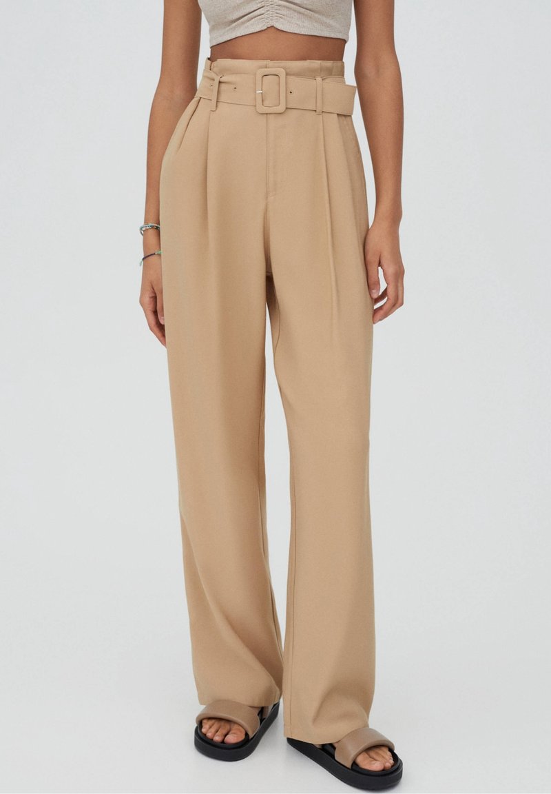 Pantalons beiges taille haute avec jambes larges, dotés d'une ceinture à l'avant et de plis. Fabriqués dans un tissu lisse avec un design épuré et taillé.