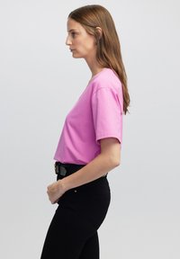 Lichtroze T-shirt met korte mouwen, een relaxed fit, ronde halslijn en een zachte textuur, gecombineerd met hoge zwarte jeans.