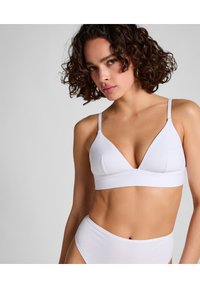 Bralette blanco de algodón suave con un diseño triangular, tirantes finos y una banda sin costuras. Presenta un ligero acolchado y una estética minimalista.