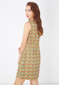 Vestido sin mangas de tela marrón que presenta un colorido patrón de hojas. Forma en A, con una textura suave y un diseño a la altura de la rodilla.