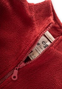 Rote Fleece-Jacke mit hohem Kragen und einem rosa Reißverschluss. Weicher Stoff und Pflegeetikett sichtbar im Kragen. Größe 2-3 Jahre.