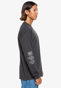 Long-sleeve gray T-shirt made of cotton. Features white graphics on the left sleeve. Casual fit with a round neckline.