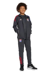 Zwart sportief trainingspak met rode en blauwe accenten, voorzien van een embleem op de linker borst en bijpassende broek met gestreept detail.