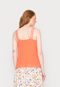 Top laranja sem mangas com alças de renda, apresentando um design fluído e bainha em camadas, combinado com uma saia de padrão floral.
