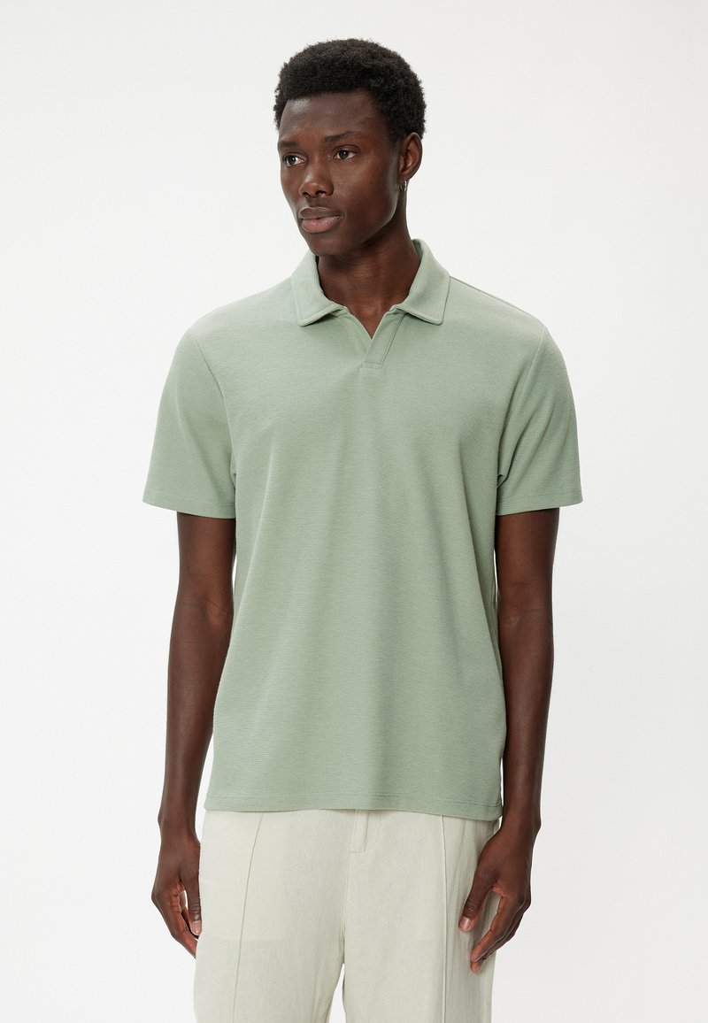 Lys grøn kortærmet polo-shirt med tekstureret stof, klassisk krave og lige kant. Bæres med lyse bukser.