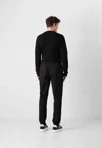 Zwarte geribbelde trui gecombineerd met zwarte cargobroek met elastische enkelmanchetten en zijzakken, aangevuld met zwart-witte sneakers.