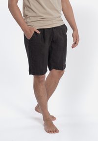 Czarne lniane szorty z dwoma bocznymi kieszeniami, podwiniętymi mankietami i luźnym krojem, w połączeniu z beżową koszulką z okrągłym dekoltem. Noszone na boso.