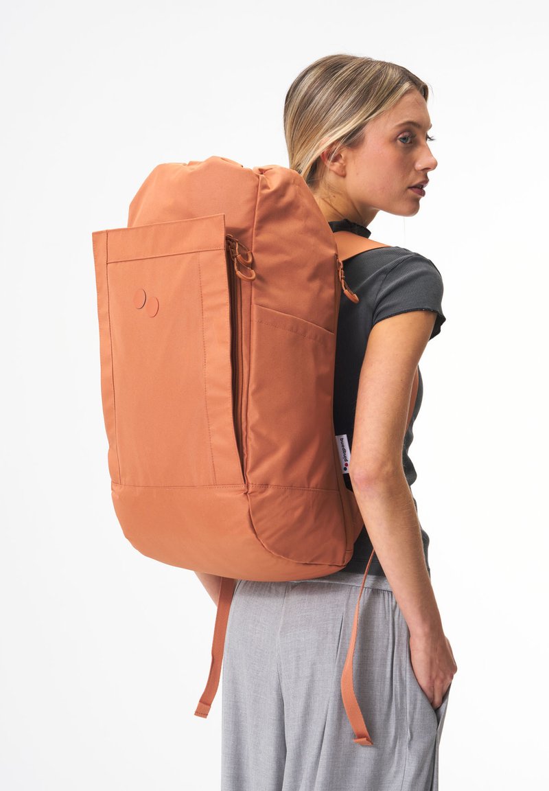 Oranger Rucksack aus strapazierfähigem Material, mit einer seitlichen Reißverschlusstasche, verstellbaren Trägern und runder Form. Glatte Textur mit minimaler Gestaltung.