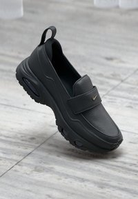 Μαύρο δερμάτινο παπούτσι τύπου slip-on με επενδυμένο κολάρο, στρογγυλεμένη μύτη και λουράκι με βέλκρο. Διαθέτει παχύ καουτσούκ πέλμα με αερόσολα. Χρυσή λεπτομέρεια με λογότυπο.