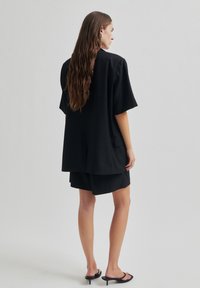 Černý oversized blazer s krátkými rukávy, spárovaný s odpovídajícími černými šortkami. Vyrobeno z hladké látky, s čistými liniemi a minimálními kapsami.