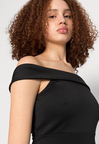 Vestido preto sem ombros feito de tecido suave. Apresenta uma silhueta ajustada, ligeiro brilho e um design minimalista sem padrões visíveis.