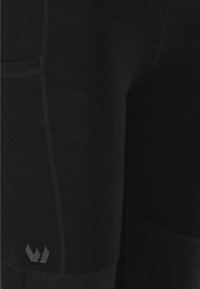Leggings de sport noirs avec une texture lisse, une coupe ajustée, des coutures renforcées et un détail de logo près de l'ourlet.