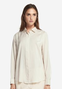 Camicia a maniche lunghe, con bottoni, di colore crema con sottili righe verticali. Presenta un colletto classico e una texture morbida e liscia.