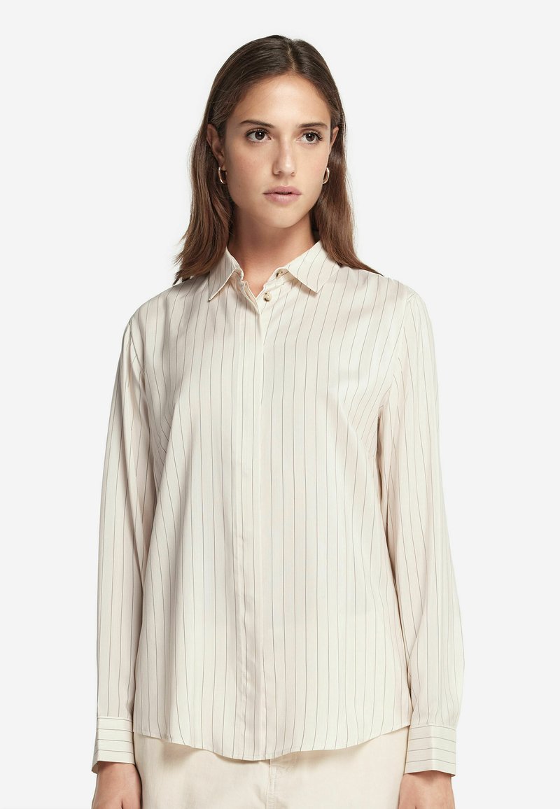 Camicia a maniche lunghe, con bottoni, di colore crema con sottili righe verticali. Presenta un colletto classico e una texture morbida e liscia.