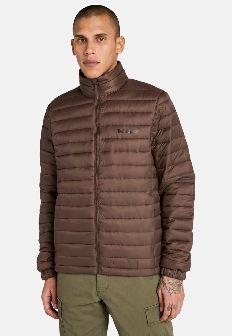 Brun puffjacka med kviltat mönster, hög krage och dragkedjestängning. Har elastiska ärmslut och Timberland-logotyp på bröstet.