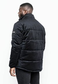 Zwarte, gewatteerde jas met een staande kraag, textuur stof, zijzakken en een logo op de linker mouw. Slanke pasvorm.