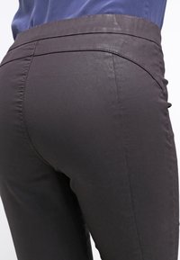 Svarta stretchbyxor i tyg med slät yta, med en figursydd design och midjehögt resår. Bakifrån visar de en lätt formning.