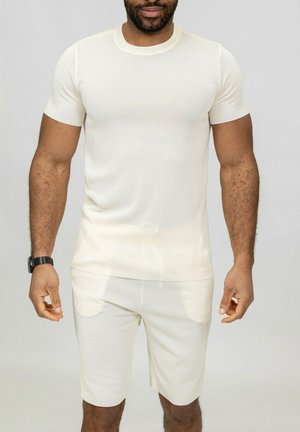 Chemise à manches courtes côtelée crème et short assorti, présentant un design ajusté, une texture douce et deux poches avant sur le short.