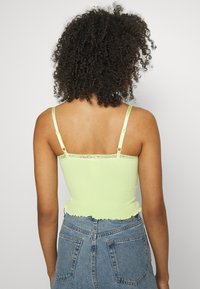 Top cropped canelado em verde néon com acabamento em renda. Apresenta alças ajustáveis e uma bainha ondulada. Combinado com calções de ganga.