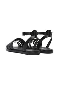 Sandales en cuir noir avec plusieurs lanières, une semelle plate et une boucle de cheville réglable. Texture lisse avec un design minimaliste.