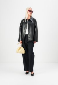 Black leather jacket with a glossy finish, white top, black wide-leg pants, and a small beige bag. Accessories include rectangular red sunglasses.