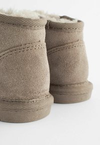 Bruna mockaskinnsankelboots med en mjuk, fluffig innerfoder, rund tå och texturerad sula. Synlig söm och släta, sömlösa kanter.
