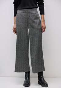 Lepakot levele mit firkanta mustriga must-valge tooniga, millel on kõrge vöökoht ja tekstureeritud kangas, koos mustade pahkluupüksidega.