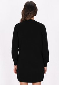 Schwarzes Strickkleid mit langen Ärmeln, gerippter Textur, rundem Hals und lockerer Passform, das hinten bis zur Mitte des Oberschenkels reicht.
