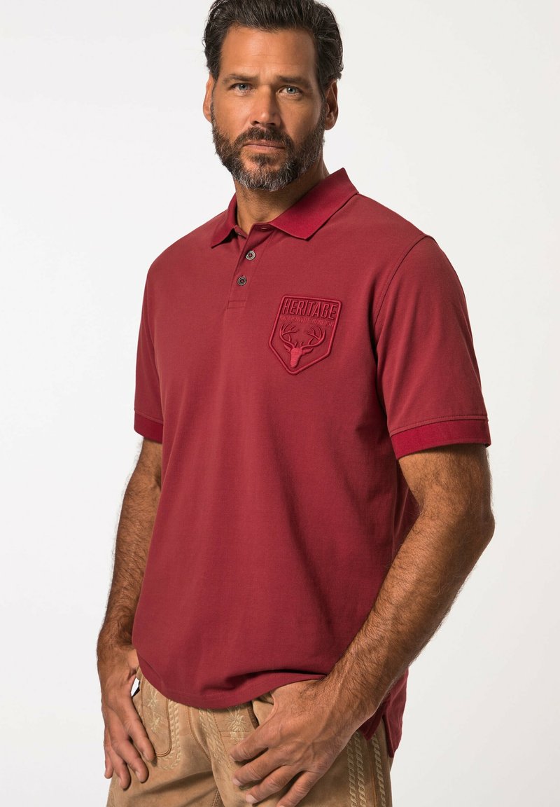 Burgundské polo tričko se třemi knoflíky, krátkými rukávy a texturovanou nášivkou se designem jelena na levé hrudi. Měkký bavlněný materiál.