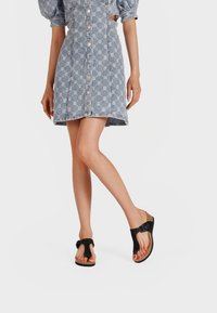 Zwarte flip-flopsandalen met een brede band en een gespsluiting, een gestructureerde voetbed en een kurken zool, gedragen met een denim jurk met een patroon.