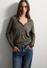 Camisa de manga larga verde oliva con cuello y detalles de botones, combinada con unos vaqueros azules de tiro alto y corte relajado.