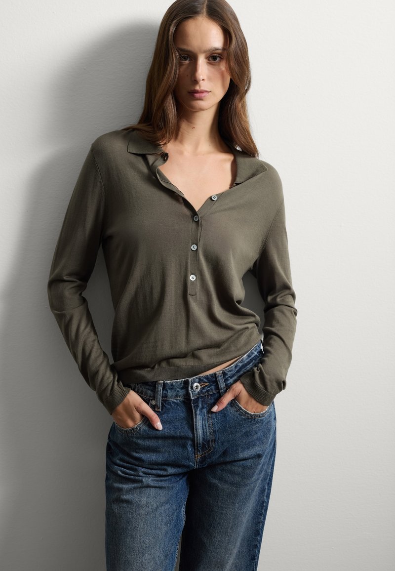 Camisa de manga larga verde oliva con cuello y detalles de botones, combinada con unos vaqueros azules de tiro alto y corte relajado.