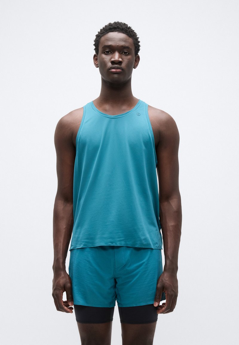 Débardeur de sport bleu sarcelle et short, fabriqués en tissu léger. Le débardeur possède un col rond ; le short est ajusté avec une ceinture élastique.