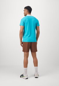 Turquoise polo shirt with short sleeves, brown shorts, and white socks. Features a contrasting collar and athletic shoes. Circular cut and breathable fabric.