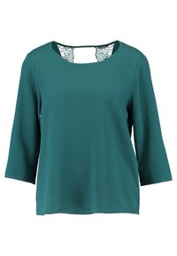 Blouse à manches longues couleur sarcelle avec encolure bateau et détail en dentelle noire au niveau de la nuque, tissu lisse et coupe décontractée.