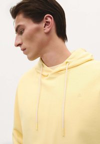 Geel hooded sweatshirt van zachte stof. Heeft trekkoorden en een klein logo. Soepele textuur met een relaxte pasvorm.