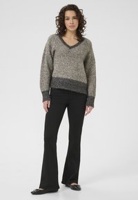 Gebreide trui met een V-hals, voorzien van een textuurpatroon in crème en grijs, gedragen met zwarte flared pants en zwarte platte schoenen.