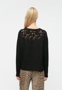 Sort langærmet top med en gennemsigtig blondebagside med blomsterbroderi, parret med leopardmønstret bukser. Blødt, afslappet stof.