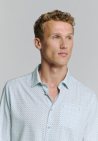 Chemise à boutons bleu clair avec motif géométrique, fabriquée en tissu tissé, dotée d'un col pointu et d'une poche poitrine unique.